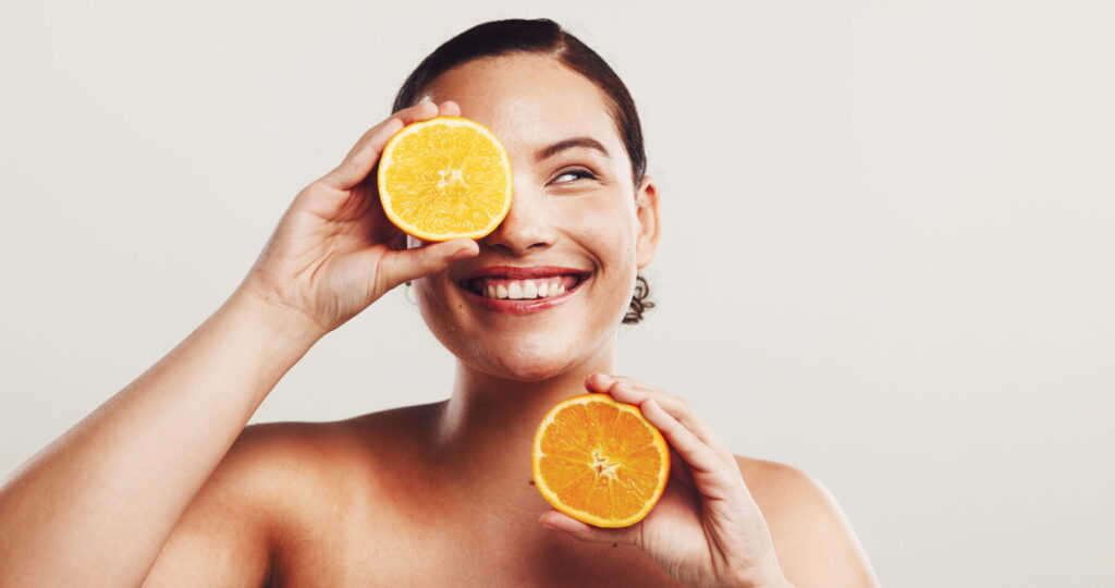 Happy woman, beauty or skincare with orange for citrus detox or vitamin C on a white studio background. Female person, model or smile with natural organic fruit for healthy skin or nutrition on space